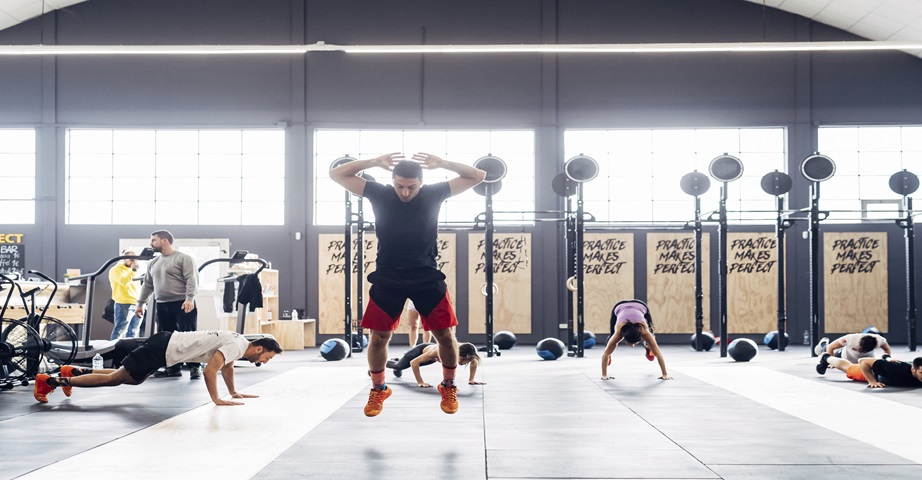 Sportowcy uprawiają burpees na sali treningowej, wykonując po kolei poszczególne etapy ćwiczenia padnij-powstań.