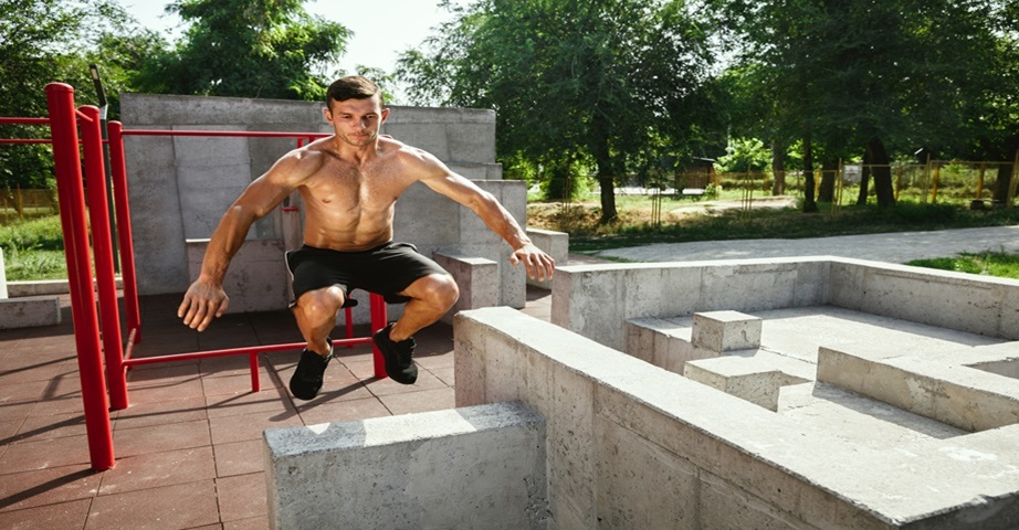 Wysportowany mężczyzna wykonuje ćwiczenia w street workout parku z barierkami i murkami 